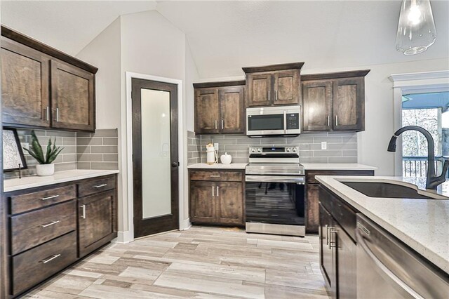 kitchen with light wood-type flooring, tasteful backsplash, appliances with stainless steel finishes, sink, and lofted ceiling