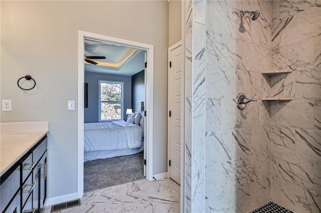 bathroom featuring a tile shower, tile patterned flooring, vanity, ceiling fan, and a raised ceiling