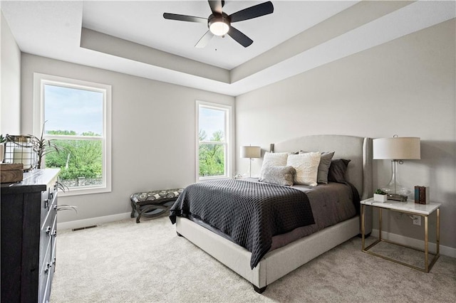 bedroom with multiple windows, a tray ceiling, and light colored carpet