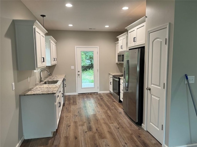 kitchen featuring appliances with stainless steel finishes, decorative light fixtures, sink, white cabinets, and wood-type flooring