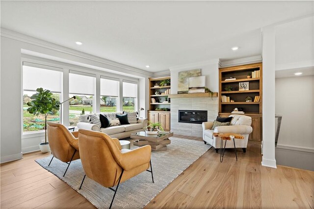 living room with light hardwood / wood-style floors, crown molding, a tiled fireplace, and built in shelves