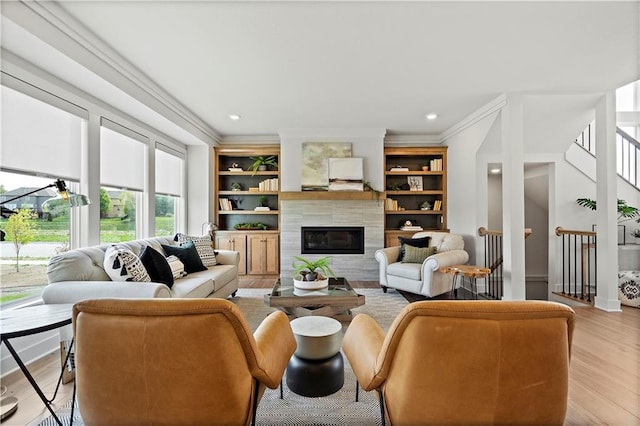 living room with a fireplace, light hardwood / wood-style floors, crown molding, and built in features