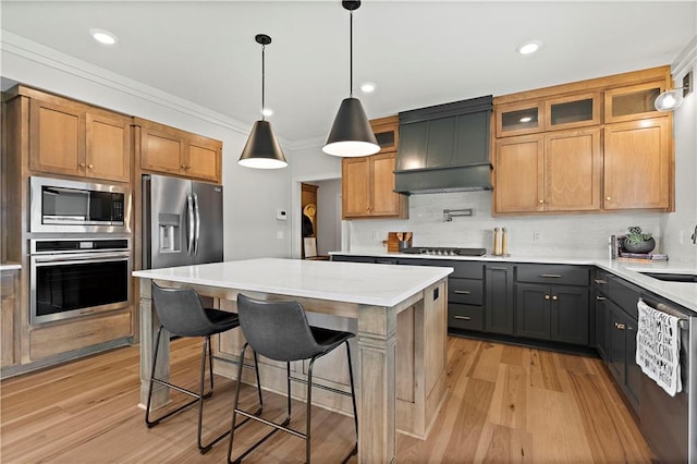 kitchen featuring premium range hood, a kitchen island, hanging light fixtures, appliances with stainless steel finishes, and light hardwood / wood-style floors