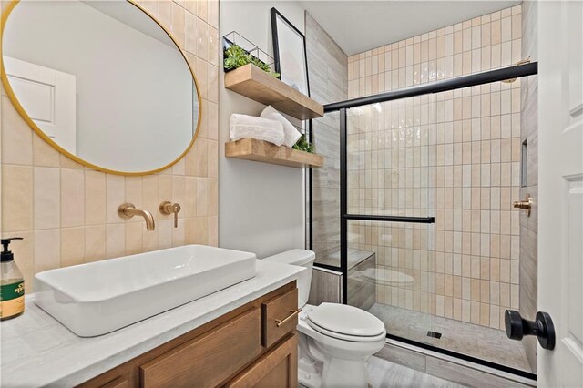 bathroom featuring a shower with shower door, tile walls, toilet, and vanity