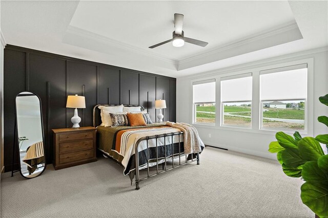 bedroom with ceiling fan, a raised ceiling, crown molding, and light carpet