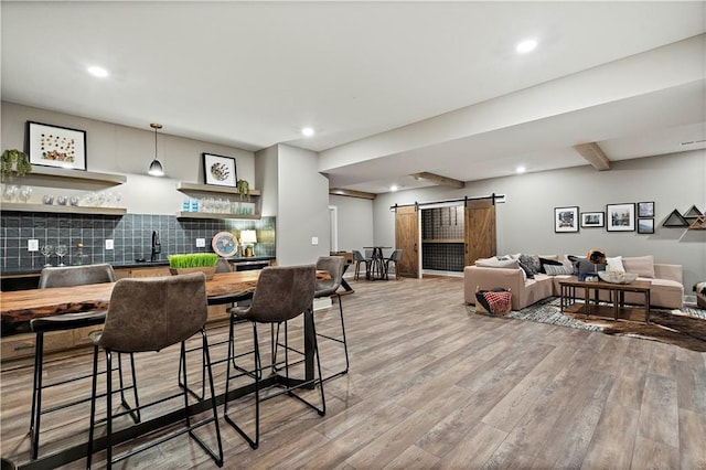 dining area featuring beamed ceiling, bar, a barn door, and light hardwood / wood-style floors