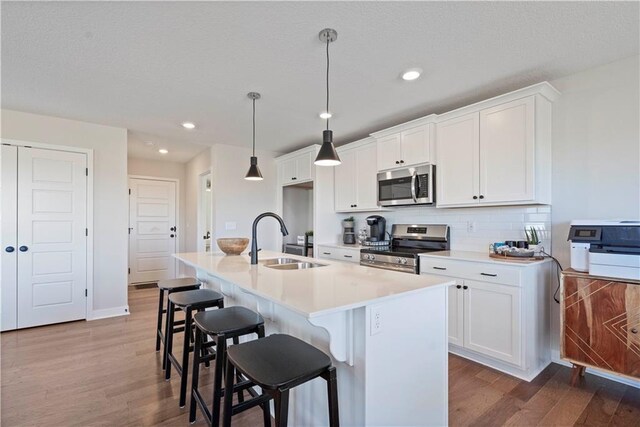 kitchen featuring sink, a center island with sink, appliances with stainless steel finishes, and wood-type flooring