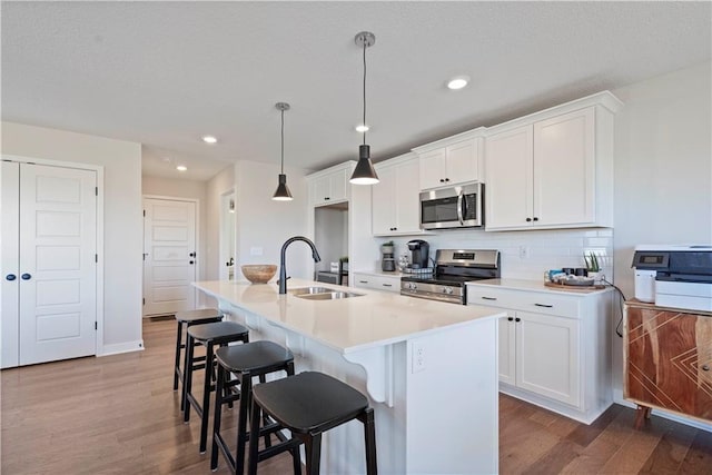 kitchen featuring an island with sink, sink, white cabinets, hanging light fixtures, and stainless steel appliances