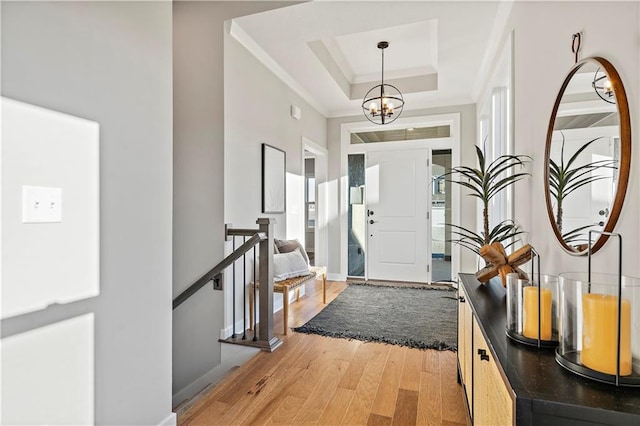 foyer entrance with hardwood / wood-style floors, ornamental molding, a raised ceiling, and a chandelier