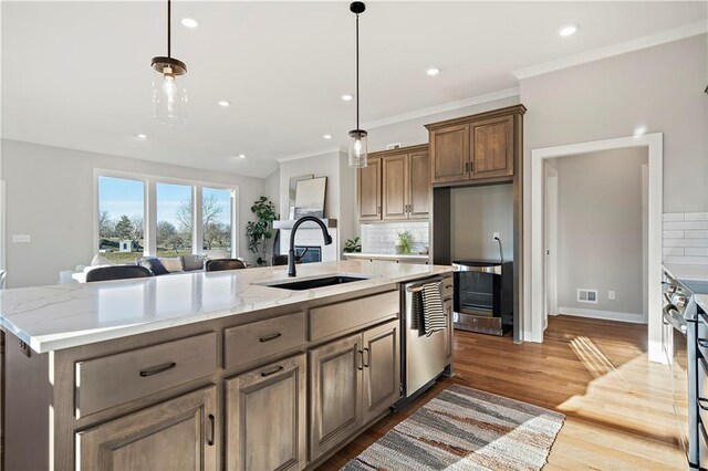 kitchen with sink, light wood-type flooring, an island with sink, and tasteful backsplash