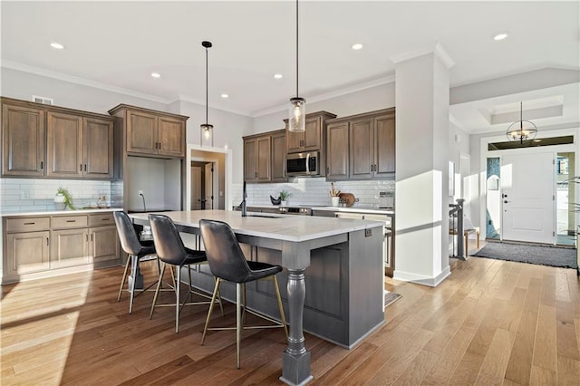 kitchen with sink, a kitchen island with sink, light hardwood / wood-style floors, a kitchen bar, and decorative light fixtures