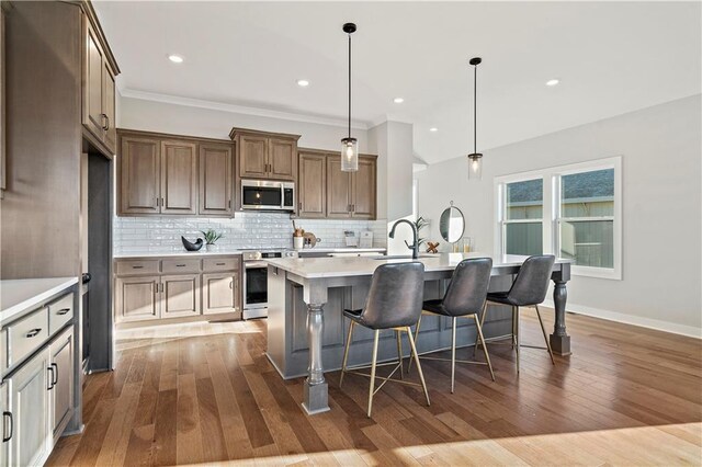 kitchen featuring a breakfast bar, backsplash, wood-type flooring, a kitchen island with sink, and pendant lighting