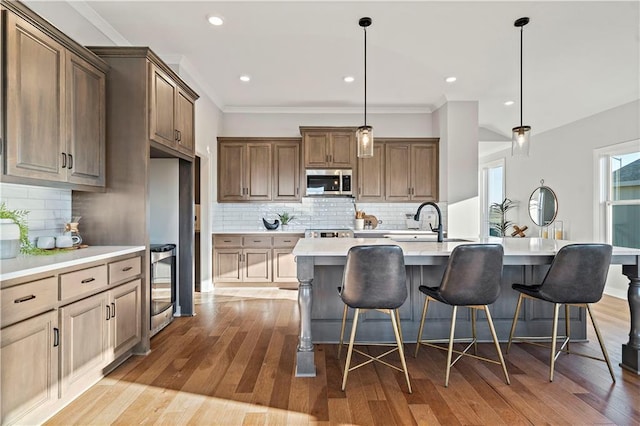 kitchen with a kitchen bar, sink, light hardwood / wood-style flooring, an island with sink, and pendant lighting