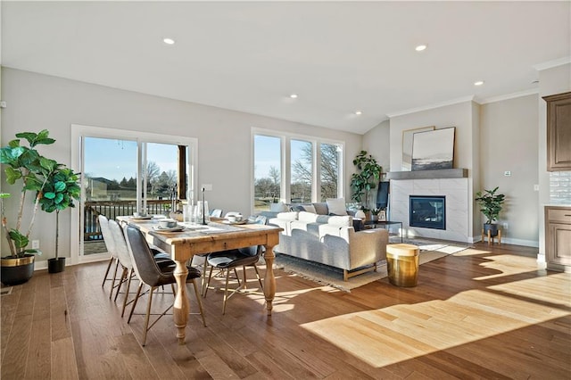 dining space with wood-type flooring, ornamental molding, and a tile fireplace