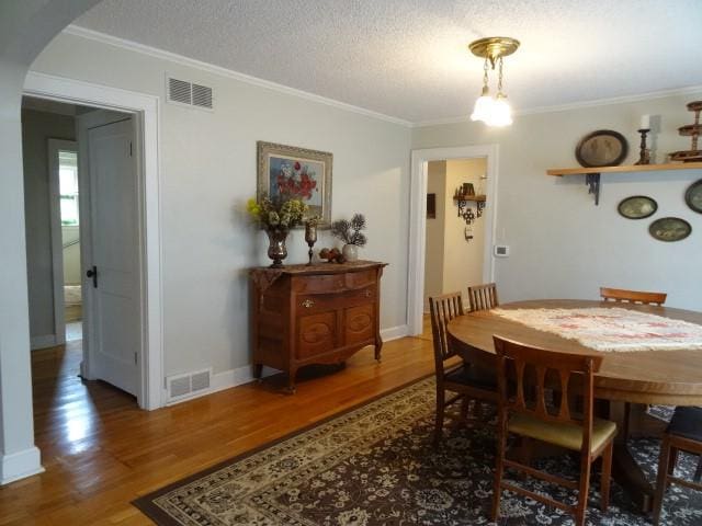 dining room with wood-type flooring, ornamental molding, and a textured ceiling