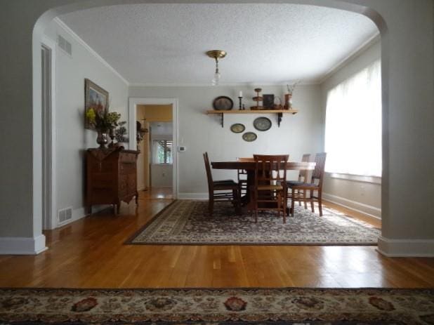 dining space with hardwood / wood-style floors, ornamental molding, and a textured ceiling