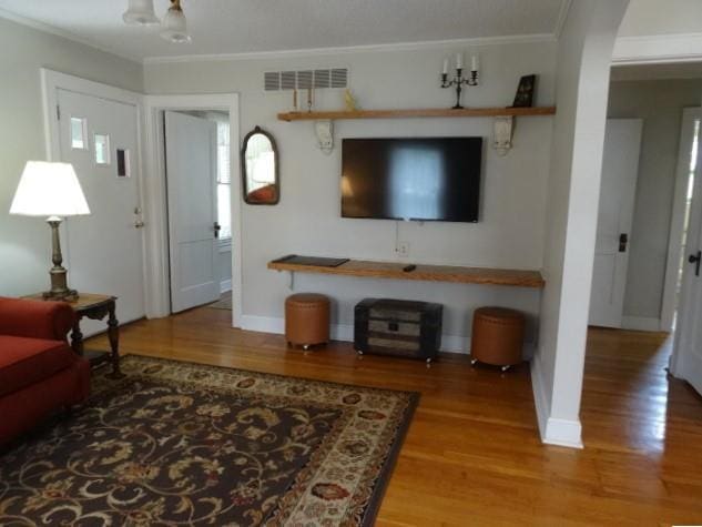 living area with ornamental molding, wood finished floors, visible vents, and baseboards