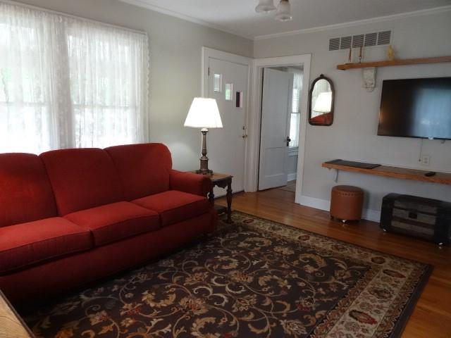 living room featuring crown molding, visible vents, and wood finished floors