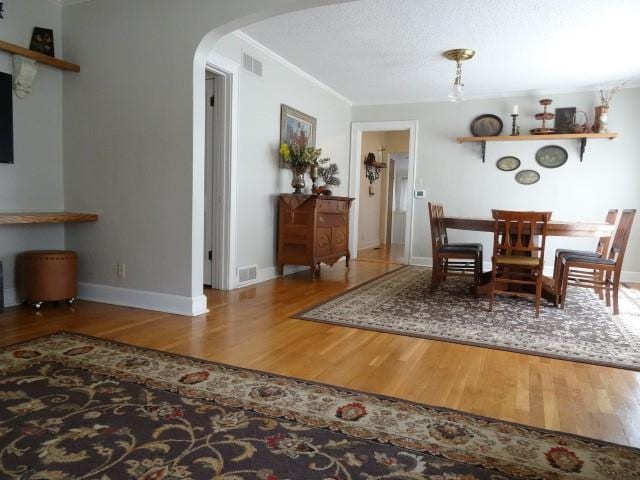 unfurnished dining area featuring baseboards, visible vents, arched walkways, wood finished floors, and crown molding