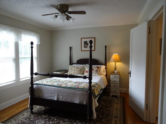 bedroom with a textured ceiling, ornamental molding, multiple windows, and wood finished floors