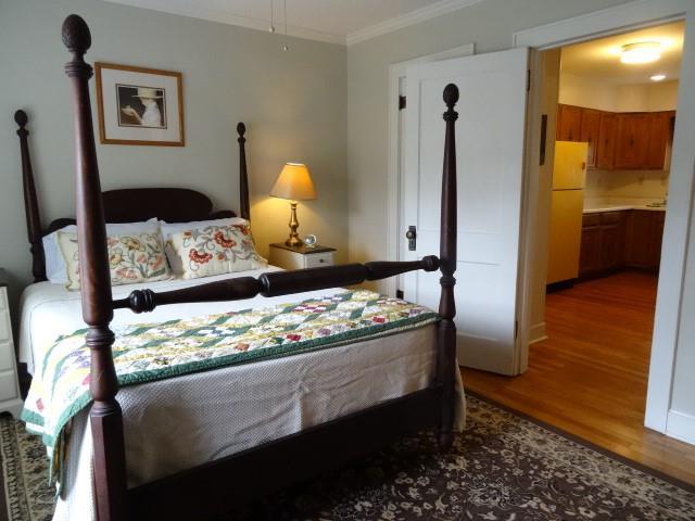 bedroom with connected bathroom, ornamental molding, hardwood / wood-style flooring, and white refrigerator