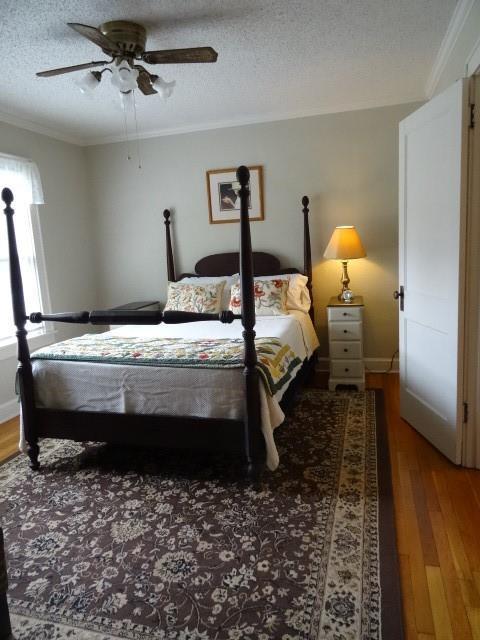 bedroom featuring a textured ceiling, wood finished floors, a ceiling fan, baseboards, and crown molding