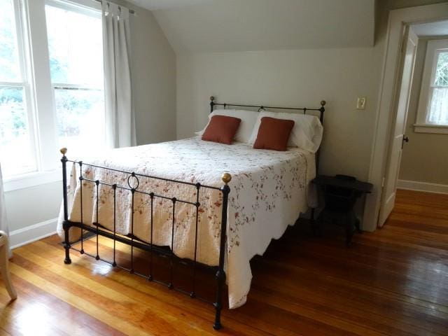 bedroom with vaulted ceiling, wood finished floors, and baseboards