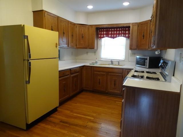 kitchen with brown cabinets, stainless steel microwave, freestanding refrigerator, a sink, and wood finished floors