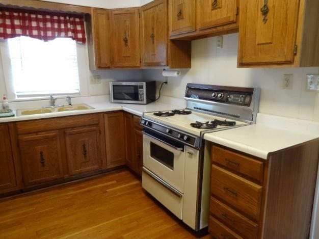 kitchen with white gas range oven, brown cabinetry, stainless steel microwave, light countertops, and a sink