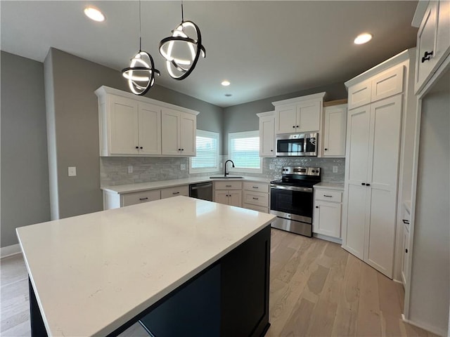 kitchen with a kitchen island, white cabinets, pendant lighting, light wood-type flooring, and appliances with stainless steel finishes