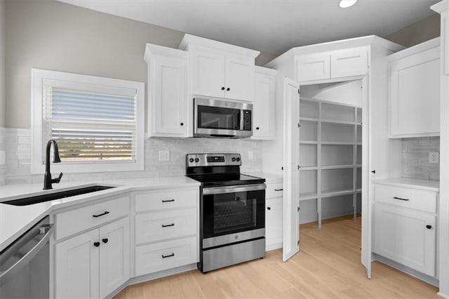 kitchen featuring white cabinets, stainless steel appliances, light countertops, and a sink