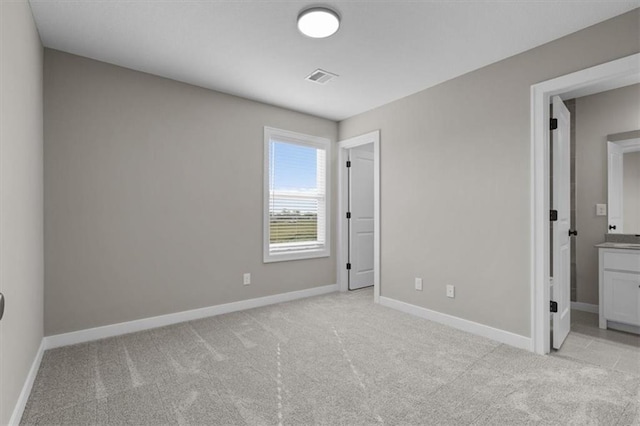 unfurnished bedroom with visible vents, light colored carpet, ensuite bathroom, and baseboards