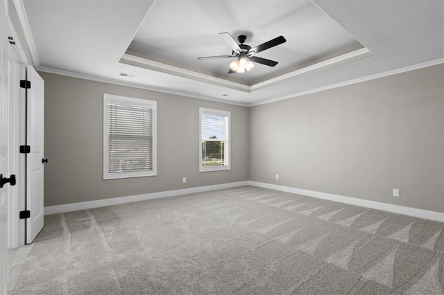 carpeted empty room with a tray ceiling, baseboards, ornamental molding, and a ceiling fan