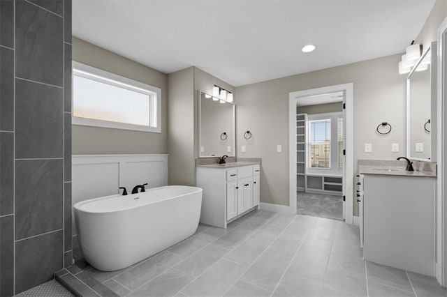 bathroom featuring a sink, a freestanding tub, plenty of natural light, and two vanities