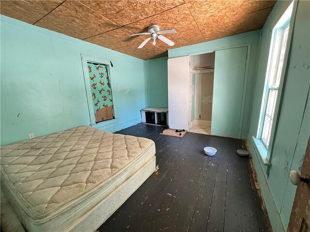 unfurnished bedroom featuring ceiling fan, a closet, hardwood / wood-style floors, and multiple windows