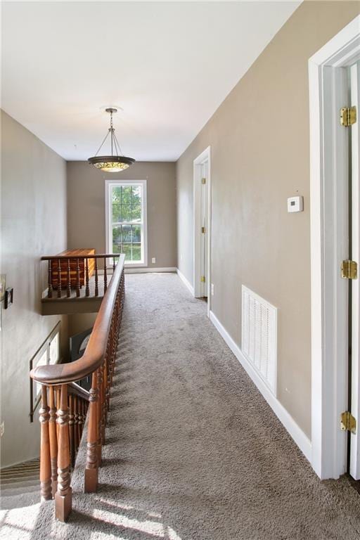 hallway with baseboards, visible vents, carpet flooring, and an upstairs landing