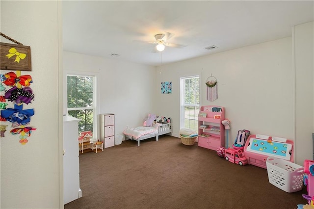 rec room with a healthy amount of sunlight, ceiling fan, visible vents, and dark carpet