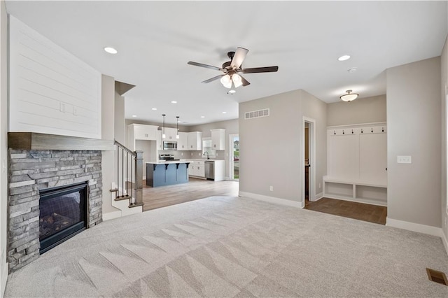 carpeted living room with ceiling fan, sink, and a stone fireplace