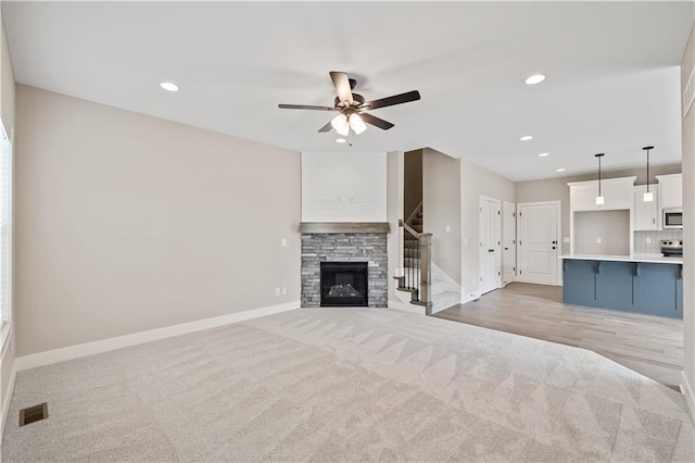 unfurnished living room featuring ceiling fan, light hardwood / wood-style floors, and a stone fireplace