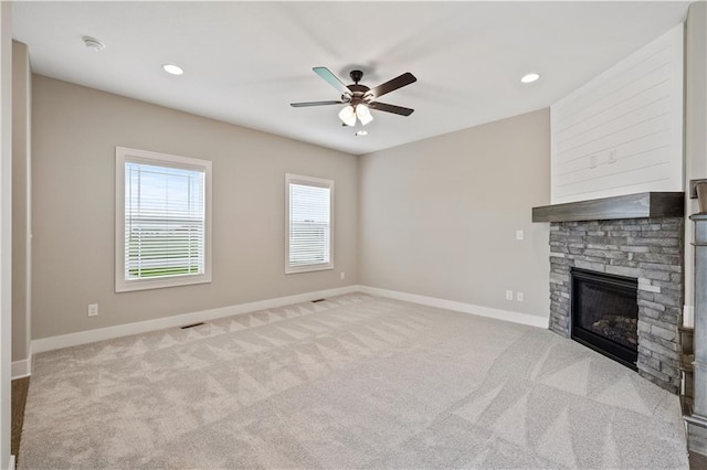 unfurnished living room with ceiling fan, a stone fireplace, and light colored carpet