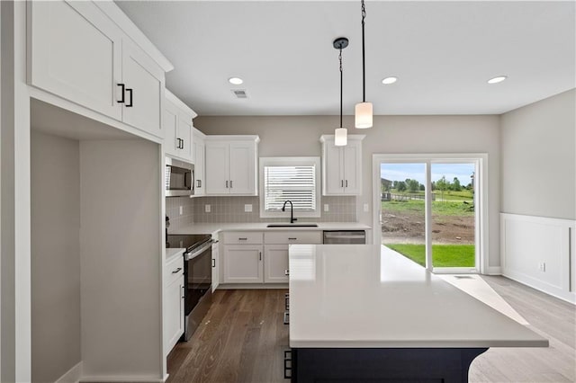 kitchen featuring dark hardwood / wood-style floors, white cabinets, sink, decorative light fixtures, and stainless steel appliances