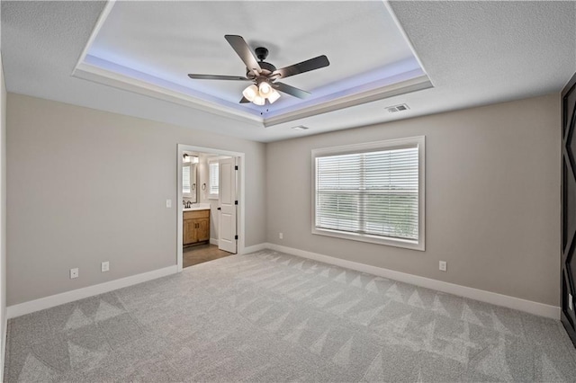 unfurnished bedroom with ceiling fan, a raised ceiling, carpet floors, and connected bathroom