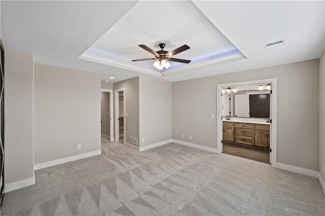 unfurnished bedroom with a tray ceiling, carpet floors, ceiling fan, and connected bathroom