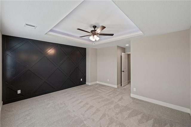 carpeted spare room with ceiling fan and a raised ceiling