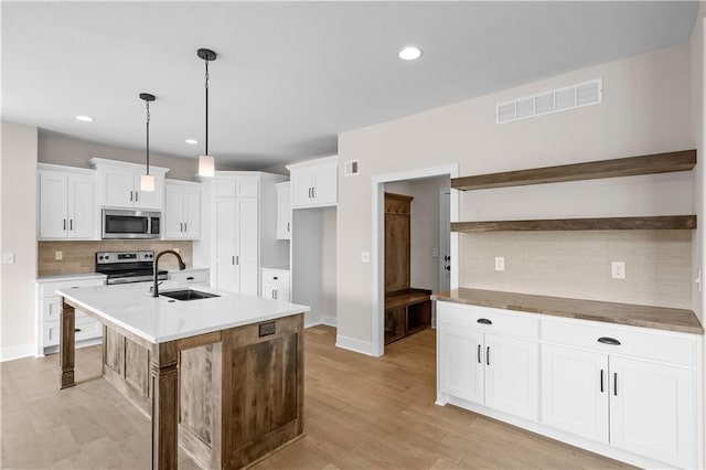 kitchen with light wood-type flooring, tasteful backsplash, an island with sink, sink, and stainless steel appliances