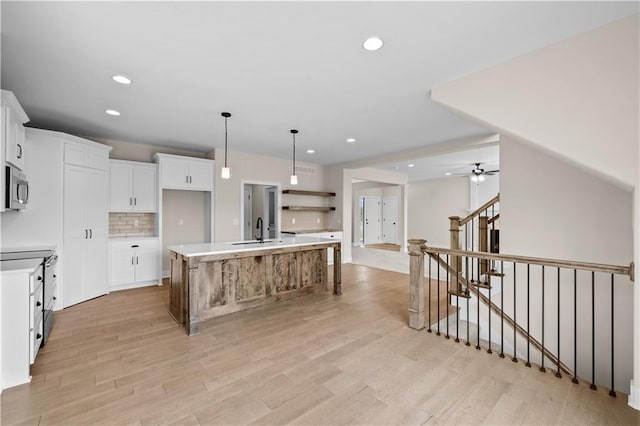 kitchen with backsplash, light hardwood / wood-style floors, white cabinetry, an island with sink, and ceiling fan