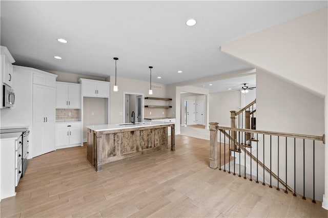 kitchen with tasteful backsplash, stainless steel microwave, a kitchen island with sink, light wood-type flooring, and a sink