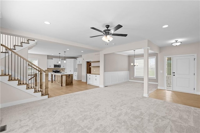 unfurnished living room with ceiling fan with notable chandelier, sink, and light colored carpet