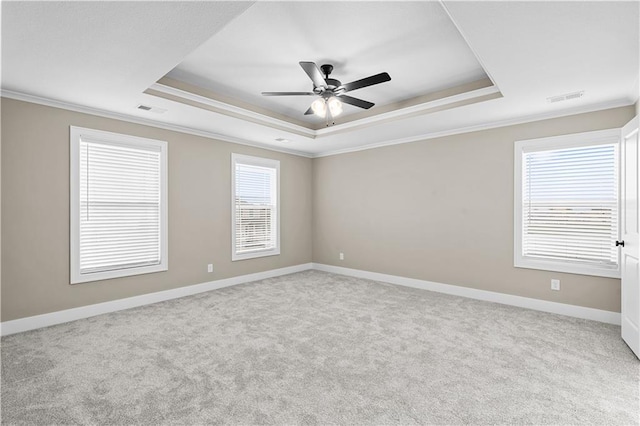 carpeted empty room featuring a raised ceiling, visible vents, crown molding, and baseboards