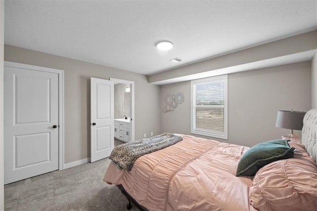 carpeted bedroom with connected bathroom and a textured ceiling